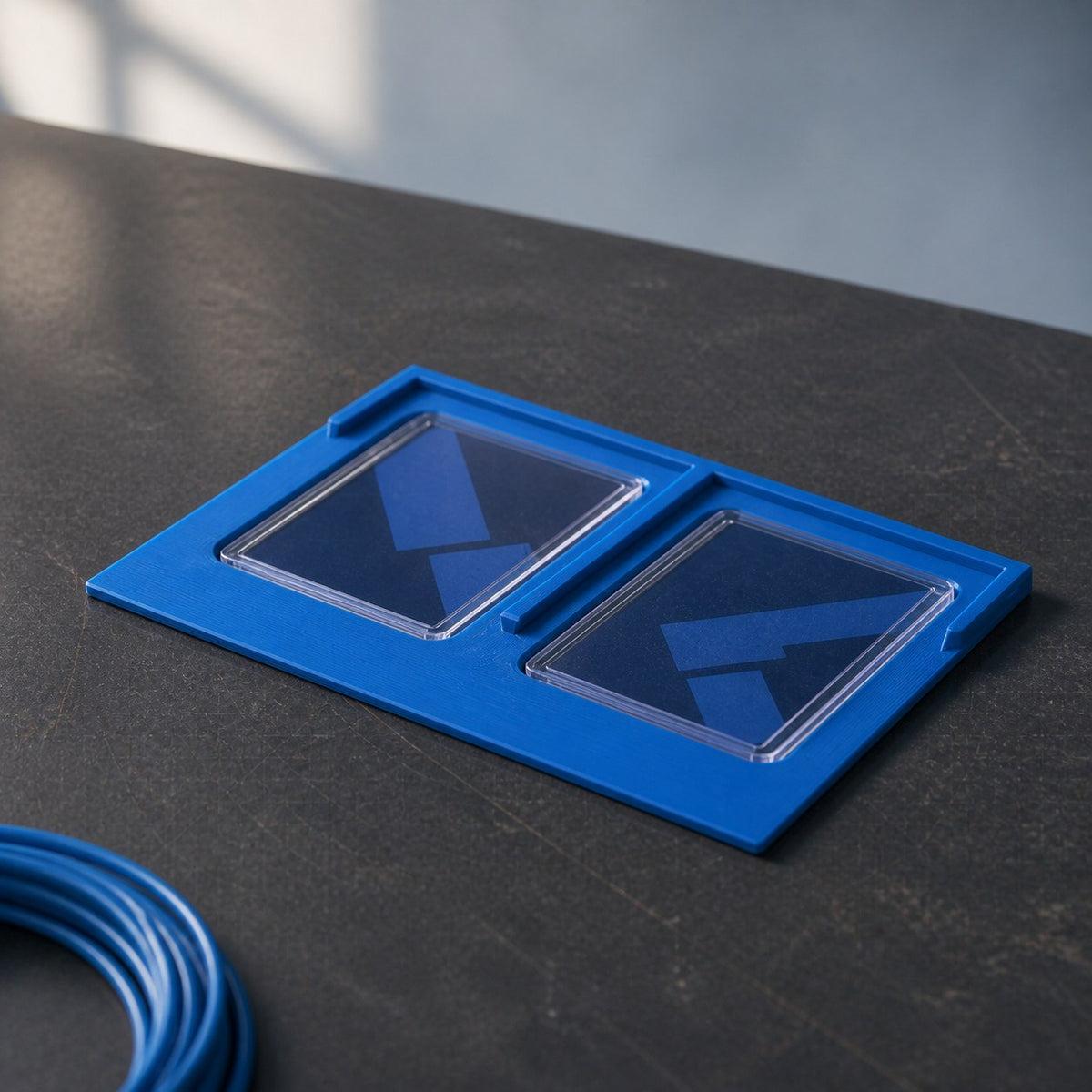 Blue 2 by 1 Toploader Holder displaying two protected cards on a maker's workbench